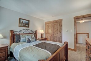 A bedroom with a wooden bed, a nightstand with a lamp, a wooden wardrobe, and a door leading to another room.