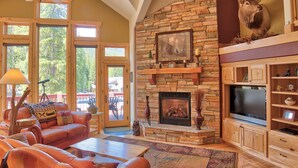 A spacious living room with a stone fireplace, a mounted deer head, and a large TV. - Moose Meadow Retreat Private Home with Hot Tub (Breckenridge)