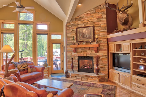 A spacious living room with a stone fireplace, a mounted deer head, and a large TV.