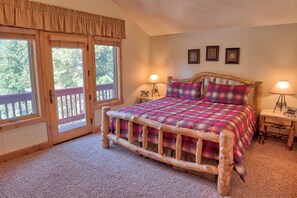 Ein Schlafzimmer mit einem Holzbettrahmen, einer Karo-Bettdecke, zwei Nachttischlampen und Blick durch eine Flügeltür.