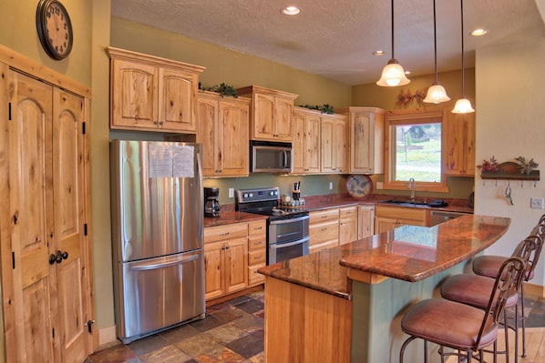 A kitchen with wooden cabinets, stainless steel appliances, a granite countertop, and bar stools.
