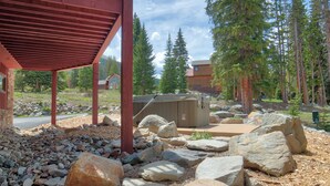 A covered outdoor area with a wooden deck, large rocks, and a building in the background. - Moose Meadow Retreat Private Home with Hot Tub (Breckenridge)