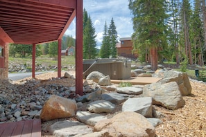 A covered outdoor area with a wooden deck, large rocks, and a building in the background.