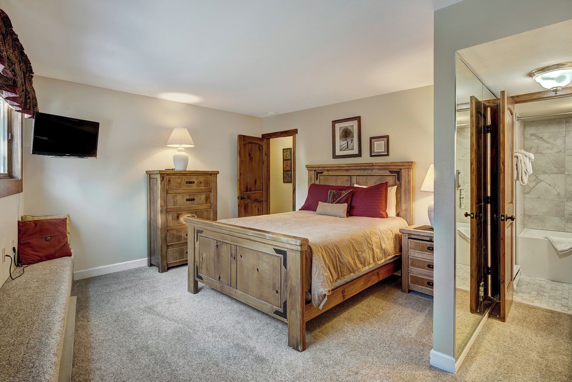 Een slaapkamer met een houten bed, een nachtkastje, een dressoir, een televisie en een badkamer met douche.