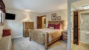 Een slaapkamer met een houten bed, een nachtkastje, een dressoir, een televisie en een badkamer met douche.