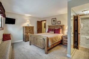 A bedroom with a wooden bed, a nightstand, a dresser, a television, and a bathroom with a shower. - Sundowner II #224 (On 4 O'Clock Rd, with on-site Hot Tub) (Breckenridge)