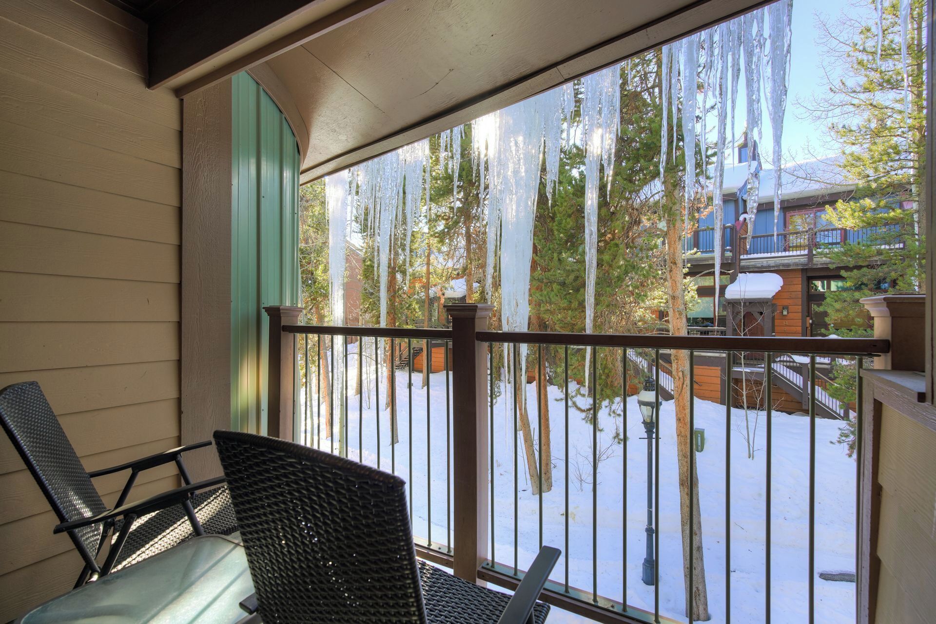 A balcony with wicker chairs, a view of a snowy landscape with trees and a building.