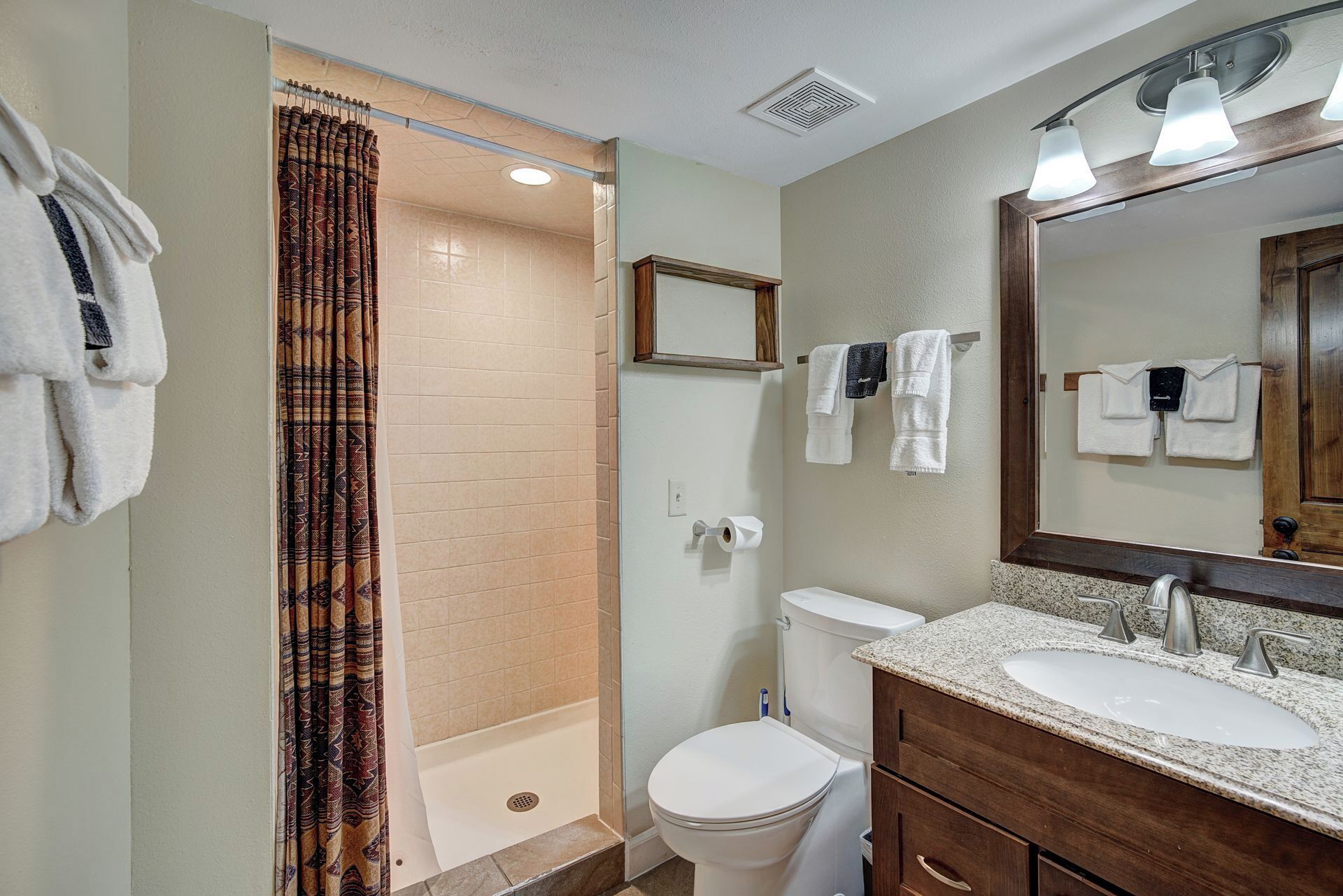 A bathroom with a shower, toilet, sink, and a mirror.