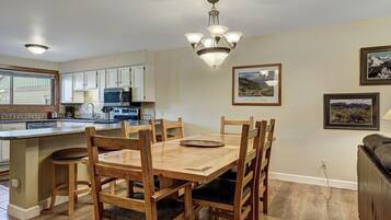 A dining area with a wooden table and chairs, a kitchen with white cabinets and appliances, and a chandelier.