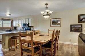 A dining area with a wooden table and chairs, a kitchen with white cabinets and appliances, and a chandelier. - Sundowner II #224 (On 4 O'Clock Rd, with on-site Hot Tub) (Breckenridge)
