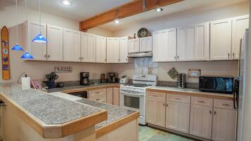 A kitchen with white cabinets, a granite countertop, a stove, a microwave, and a coffee maker.