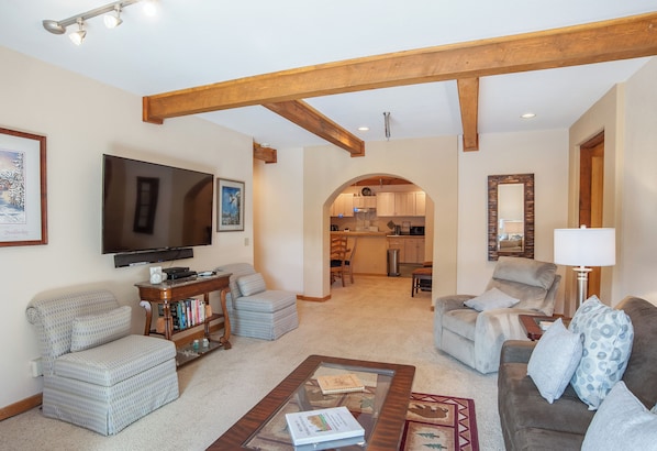 A living room with a television, seating, and a kitchen in the background.