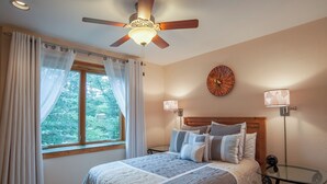 Une chambre à coucher comprenant un lit, un ventilateur de plafond, une fenêtre avec des rideaux, une horloge murale et deux lampes de chevet.