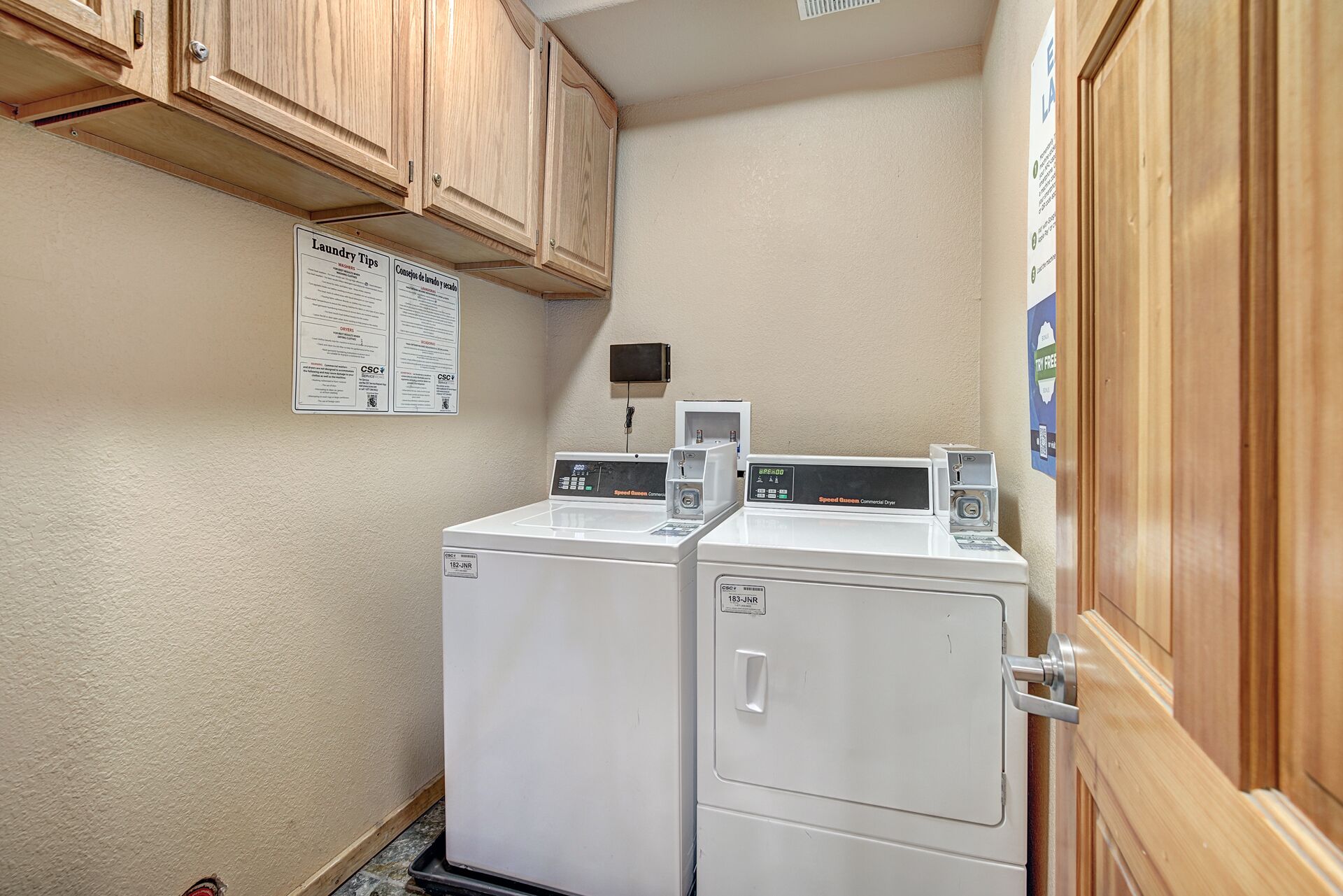 A laundry area with two white washing machines, wooden cabinets, and a bulletin board with laundry tips.