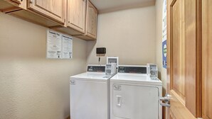 Une buanderie avec deux sèche-linge blancs, des armoires en bois au-dessus et une porte sur le côté droit.