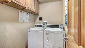 A laundry area with two white washing machines, wooden cabinets, and a bulletin board with laundry tips.