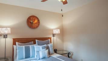A bedroom with a wooden headboard, a bed with multiple pillows, a round wall clock, two bedside lamps, and a ceiling fan.