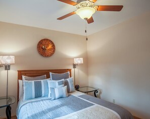 Ein Schlafzimmer mit einem hölzernen Kopfteil, einem Bett mit vielen Kissen, einer runden Wanduhr, zwei Nachttischlampen und einem Deckenventilator.