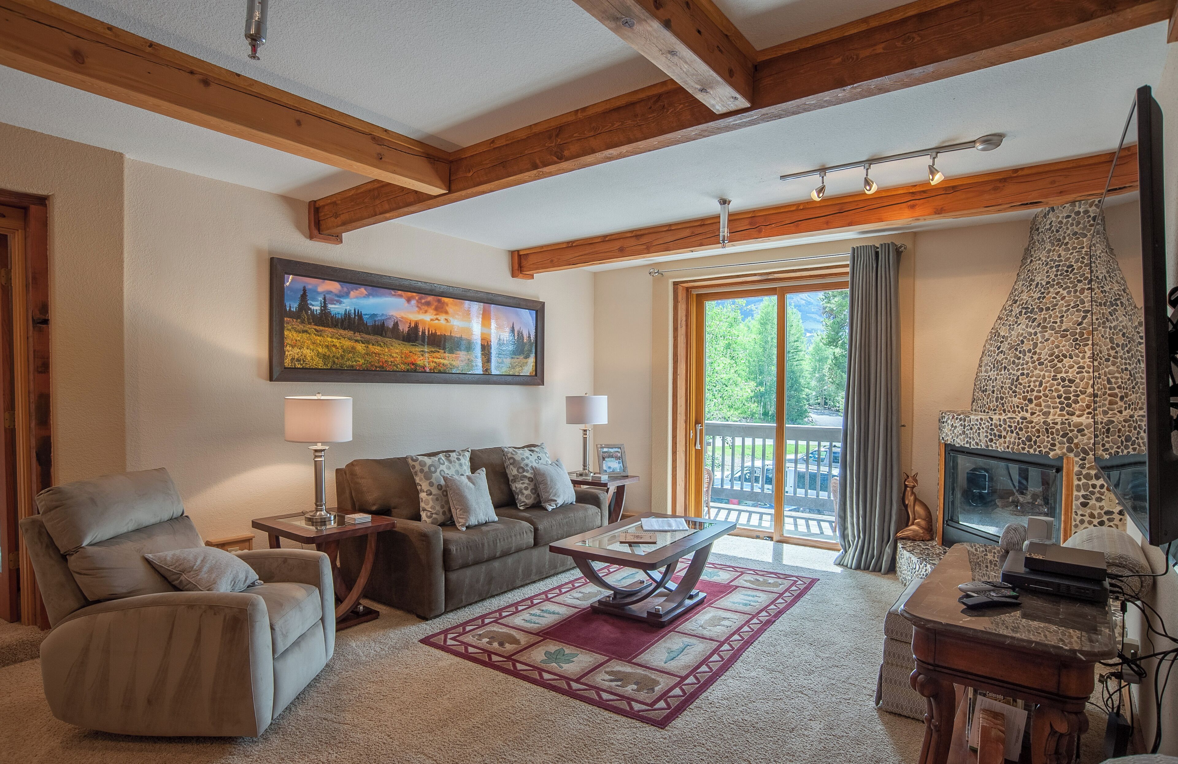 A cozy living room with a fireplace, a large window with curtains, and a painting on the wall.
