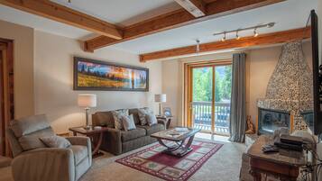 A cozy living room with a fireplace, a large window with curtains, and a painting on the wall.