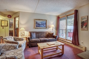 A cozy living room with a sofa, armchairs, a coffee table, and a large window with curtains.