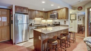 A modern kitchen with wooden cabinets, stainless steel appliances, and a central island with bar stools. - Trail's End 201 Downtown Condos with on-site Hot Tub (Breckenridge)