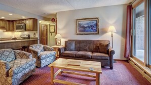A cozy living room with a brown leather sofa, patterned armchairs, and a wooden coffee table. A painting hangs on the wall, and there is a window with curtains. - Trail's End 201 Downtown Condos with on-site Hot Tub (Breckenridge)