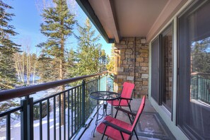 A balcony with a stone wall, two red chairs, and a small round table.