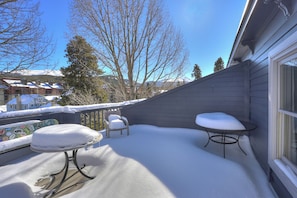 Une terrasse enneigée avec une table et des chaises, une fenêtre et une vue sur une montagne et des bâtiments en arrière-plan.