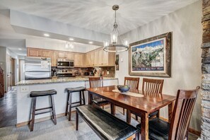 A modern kitchen with wooden cabinets, stainless steel appliances, and a dining area with a wooden table and chairs. - Wellington #3 (Townhome with Private Hot Tub) (Breckenridge)