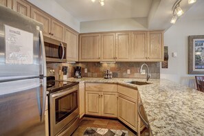 A kitchen with wooden cabinets, a stainless steel refrigerator, a microwave, an oven, a coffee maker, and a granite countertop. - Wellington #3 (Townhome with Private Hot Tub) (Breckenridge)