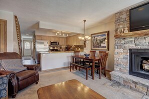 A spacious living area with a fireplace, a dining table, and a kitchen in the background.