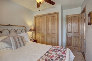 Une chambre à coucher comprenant un lit, une table de chevet, une lampe, un ventilateur de plafond et des portes en bois.