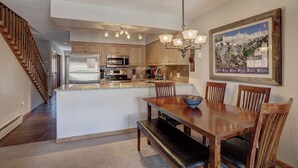 A kitchen with wooden cabinets, stainless steel appliances, a dining area with a wooden table and chairs, and a staircase on the left. - Wellington #3 (Townhome with Private Hot Tub) (Breckenridge)
