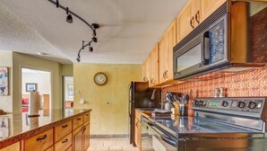 Une cuisine avec des meubles en bois, un four à micro-ondes en acier inoxydable, une cuisinière et une horloge murale.