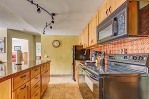 A kitchen with wooden cabinets, a stainless steel microwave, a stove, and a clock on the wall.
