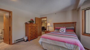 A bedroom with a bed, wooden dresser, and a mirror. - Atrium 207 Downtown Condos with on-site Hot Tub (Breckenridge)