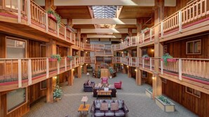 A spacious atrium with wooden balconies, a central seating area with sofas and tables, and a high ceiling with a skylight. - Atrium 207 Downtown Condos with on-site Hot Tub (Breckenridge)