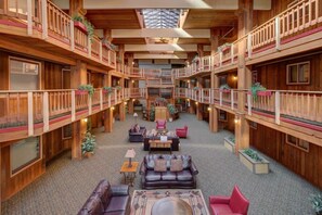 Ein geräumiger Innenhof mit hölzernen Balkonen, eine zentrale Sitzecke mit Sofas und Tischen und eine hohe Decke mit Oberlicht.