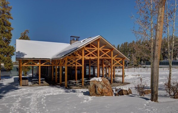 A wooden pavilion with a snow-covered roof, surrounded by snow and trees.