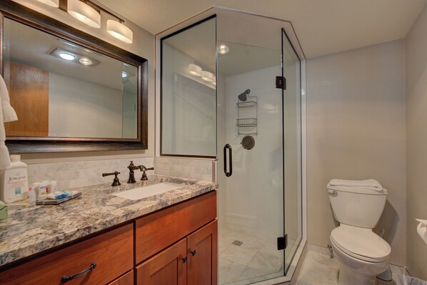 A modern bathroom with a glass-enclosed shower, a white toilet, and a granite countertop with a mirror above. - Atrium 207 Downtown Condos with on-site Hot Tub (Breckenridge)