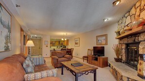 A cozy living room with a fireplace, a sofa set, a coffee table, and a television. - Atrium 207 Downtown Condos with on-site Hot Tub (Breckenridge)