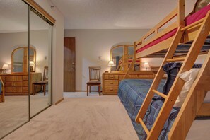 A bedroom with a bunk bed, a wooden dresser, a chair, and a mirror.