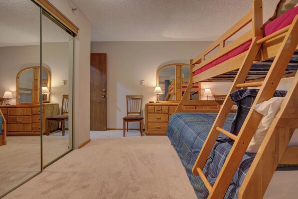 Ein Schlafzimmer mit Etagenbett, einem Holzkasten, einem Stuhl und einem Spiegel.
