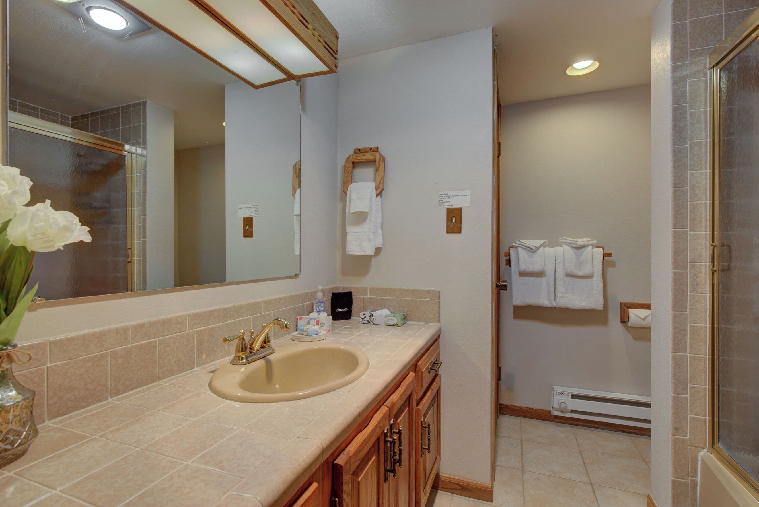 A bathroom with a sink, mirror, towel rack, and shower area.