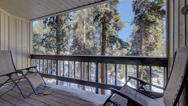 A wooden deck with two rocking chairs facing a snowy forest. - Atrium 207 Downtown Condos with on-site Hot Tub (Breckenridge)