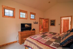 A bedroom with a large bed, a dresser, a television, and three windows.