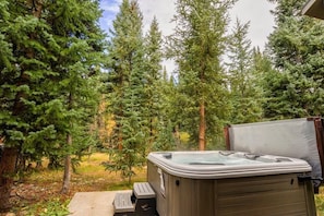 A hot tub in a forested area with tall trees and a concrete bench.