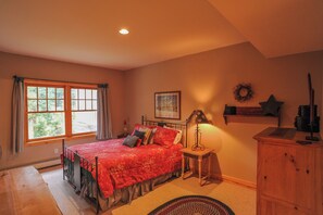 A bedroom with a large window, a bed with a red bedspread, a bedside table with a lamp, and a wooden cabinet. - 368 Settlers Drive Private Home with Hot Tub (Breckenridge)