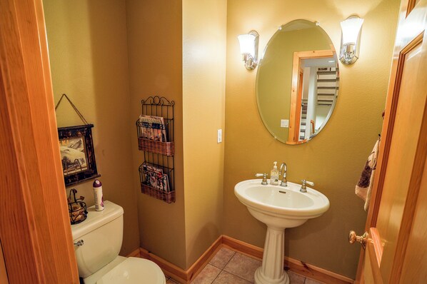 A bathroom with a toilet, a sink, a mirror, and a wall-mounted light fixture.